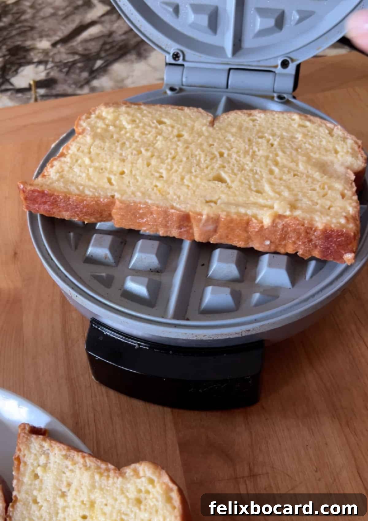 Soaked bread slice cooking inside a preheated waffle maker.