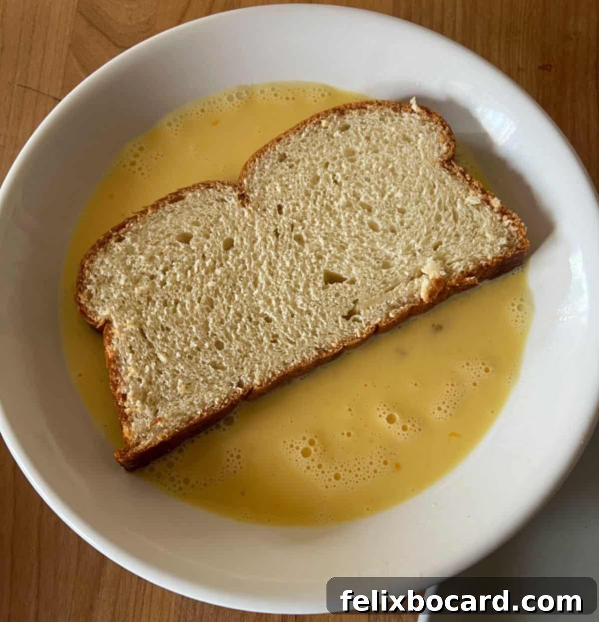 Rustic Miche bread being dipped into the egg mixture for French toast waffles.
