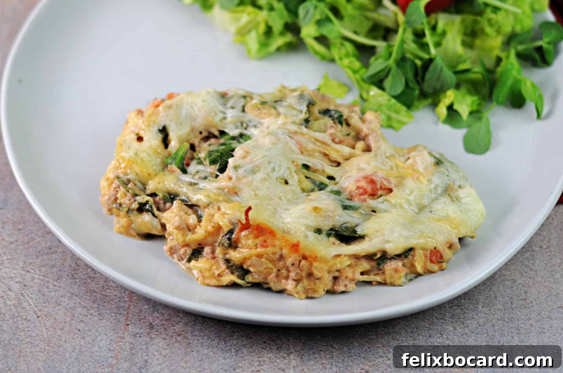 A serving of ground turkey and spaghetti squash casserole on a plate with salad, showcasing its rich, comforting appeal and vibrant colors.