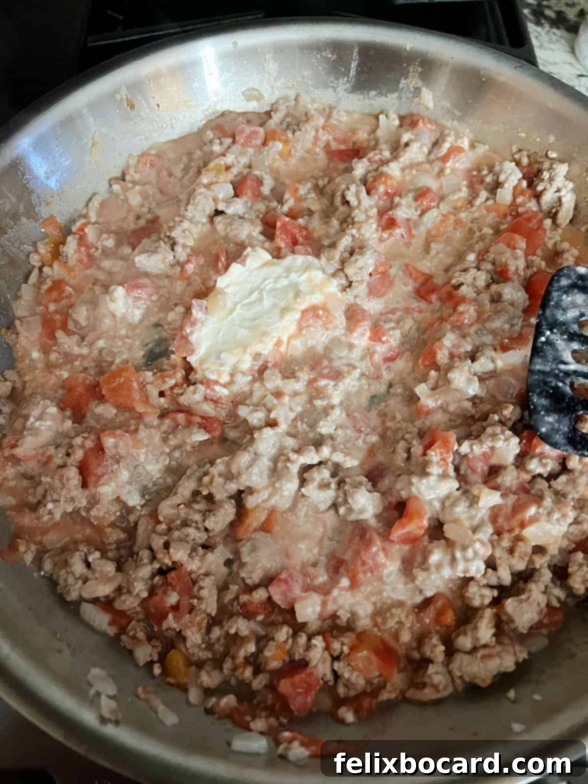Cream cheese melting gracefully into a skillet filled with cooked ground turkey and diced tomato mixture, creating a smooth and rich base for the casserole.
