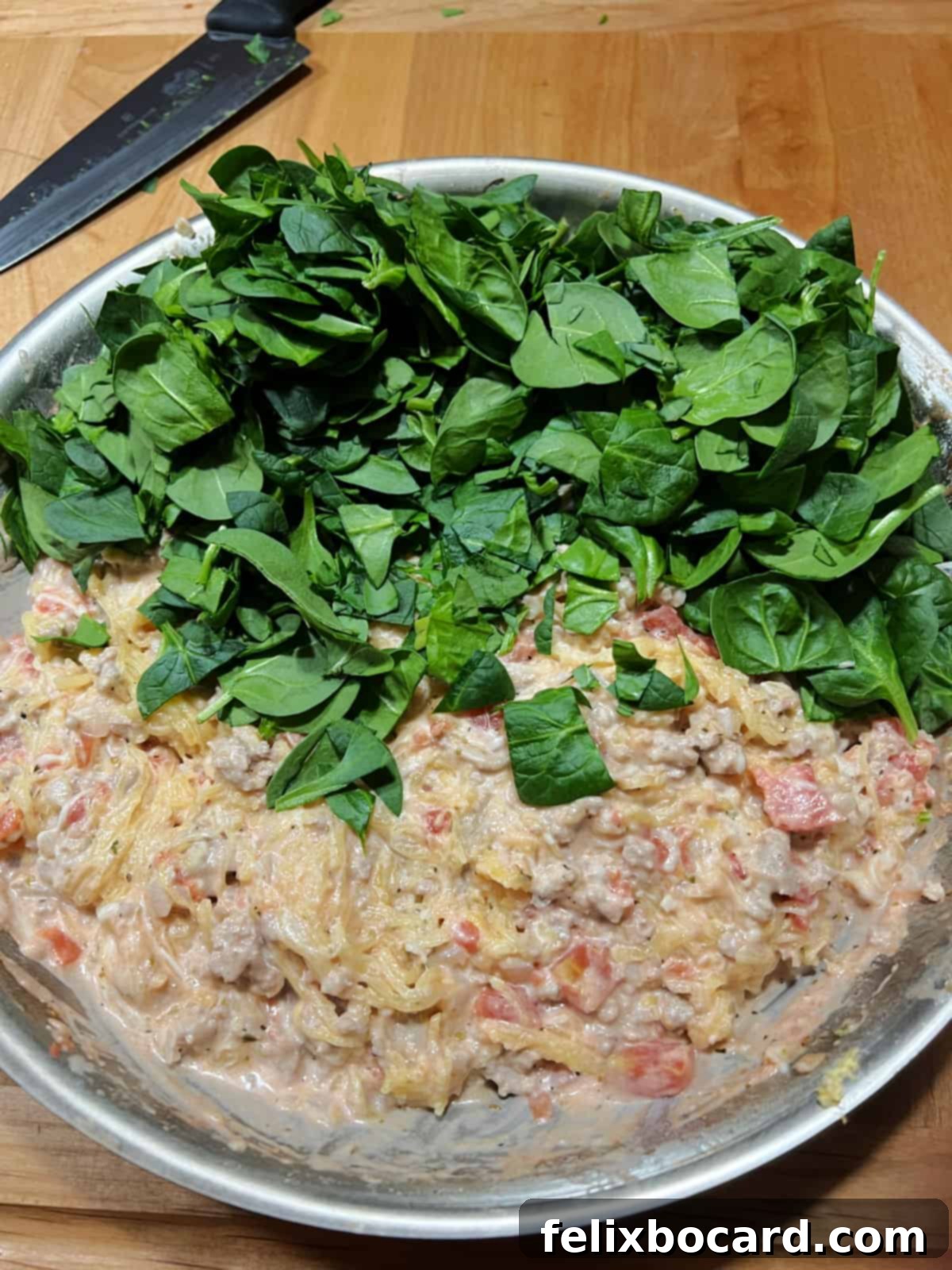 Fresh spinach being added to the hot skillet mixture, ready to wilt and integrate into the rich casserole base.