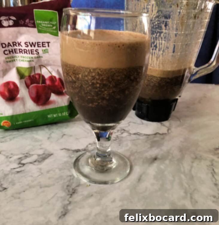 Daily Green Boost 4 brown-ish colored smoothie with blender and bag of cherries behind