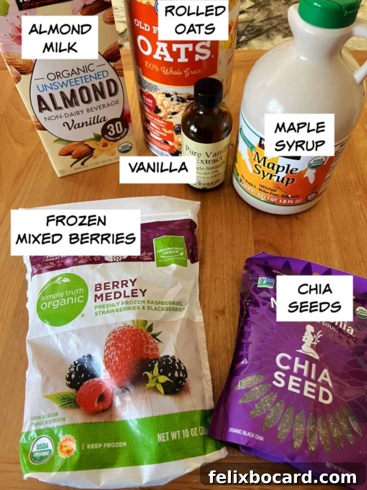 A selection of ingredients for overnight oats: almond milk, rolled oats, vanilla extract, maple syrup, chia seeds, and frozen berries.