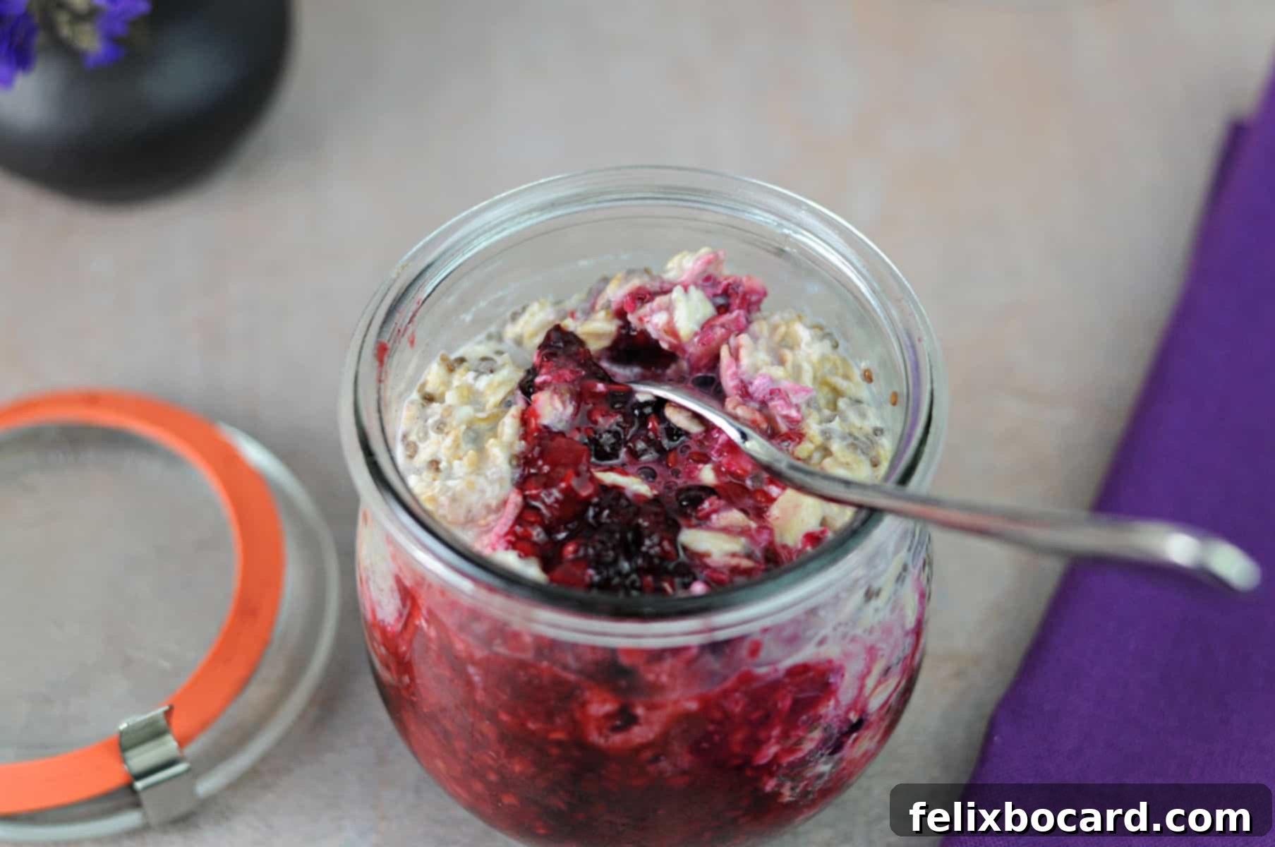A spoon stirring the layered overnight oats in a jar, bringing the fruit from the bottom up to mix with the oats.