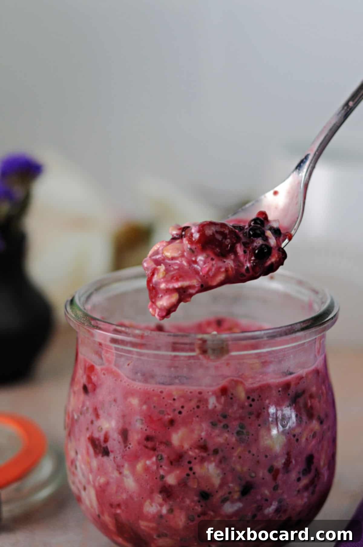A spoon suspended over a jar of mixed overnight oats, filled with fruit and ready to be eaten.