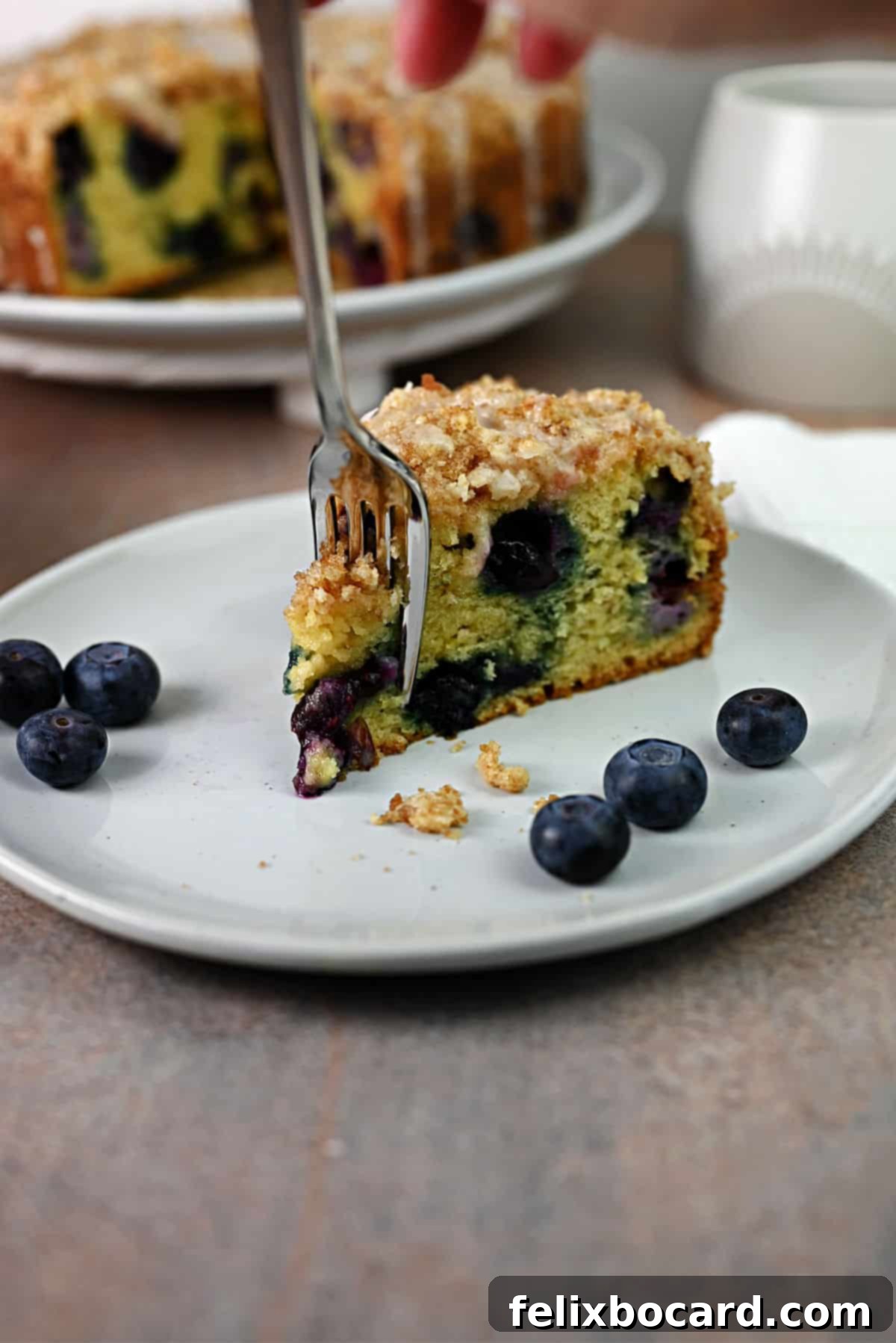 A fork cutting into a slice of blueberry sour cream coffee cake, showing its moist interior and streusel topping.