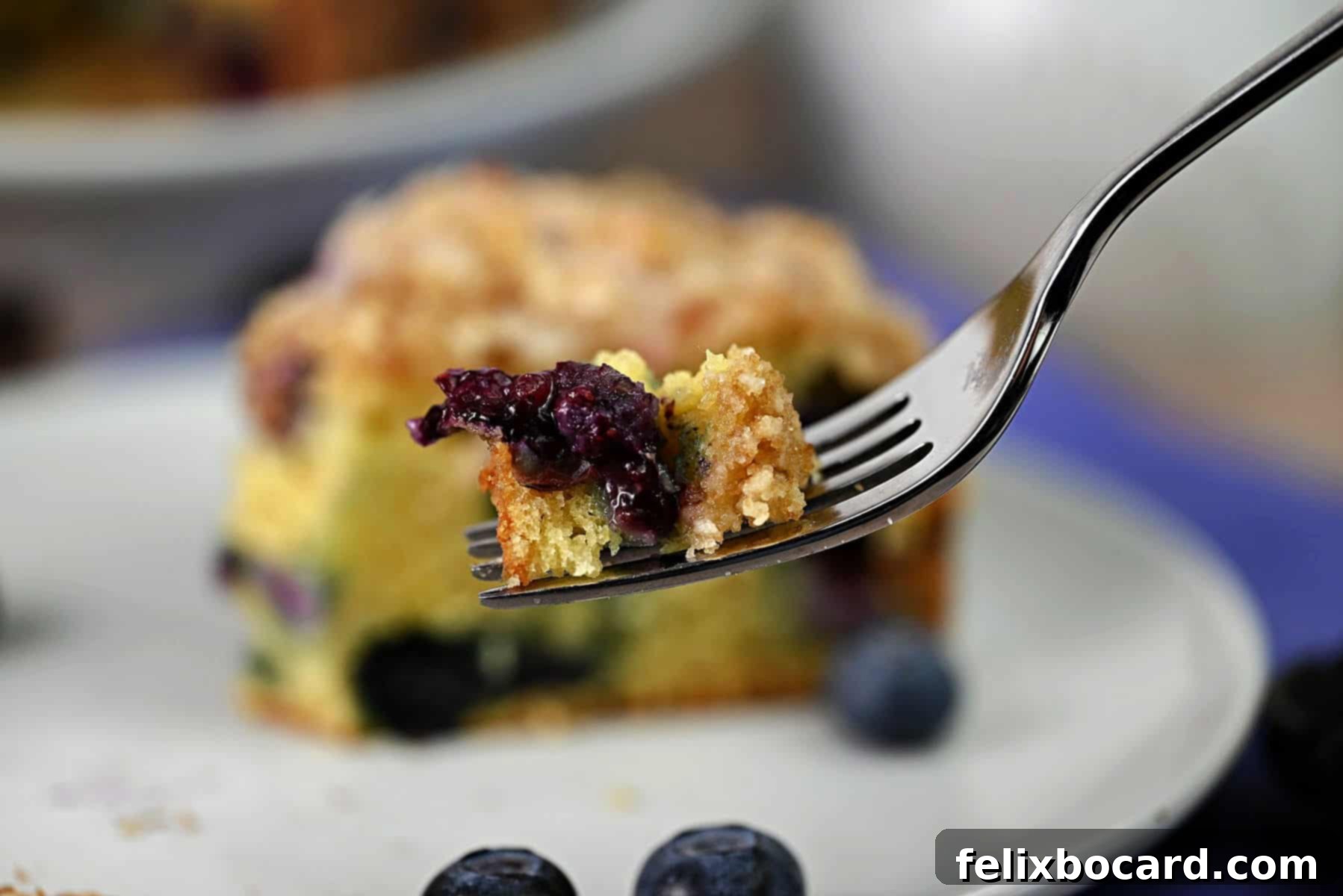 A fork holding a perfect bite of blueberry sour cream coffee cake, showing the texture and blueberries.
