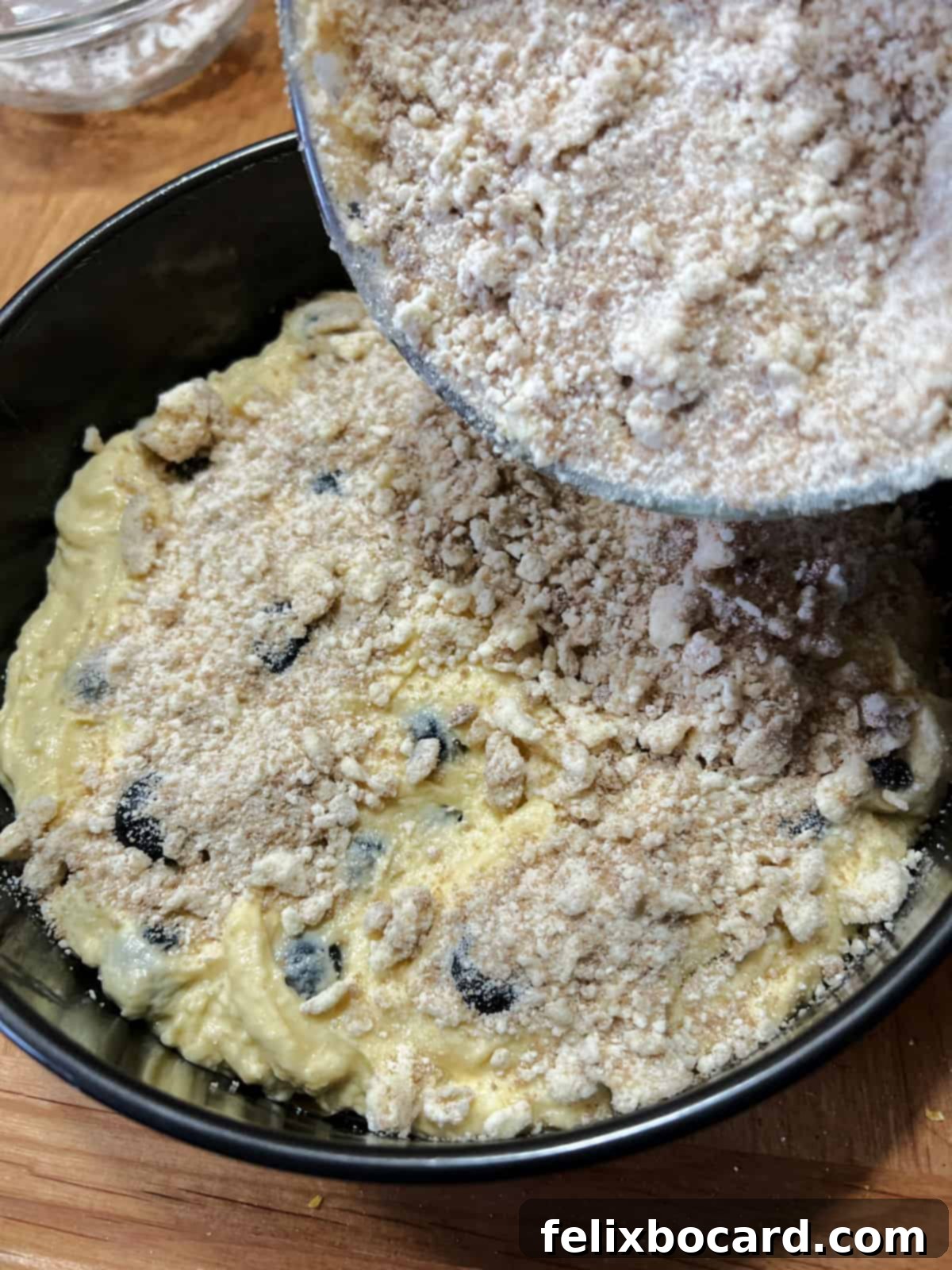 Adding streusel to the top of the blueberry sour cream coffee cake batter in the pan.