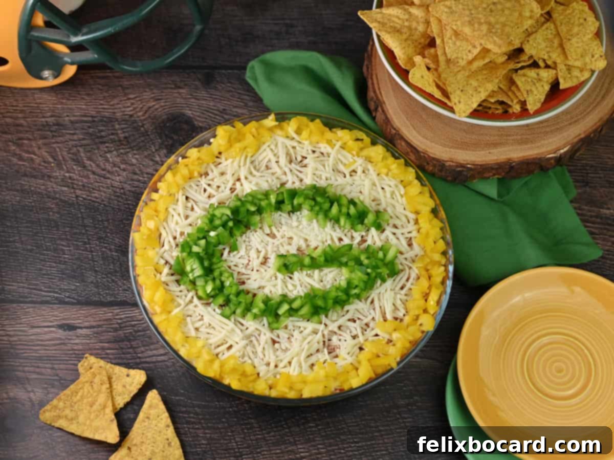 Vibrant Layered Taco Dip decorated with the iconic Green Bay Packers 'G' logo, surrounded by tortilla chips, ready to be served at a football party.