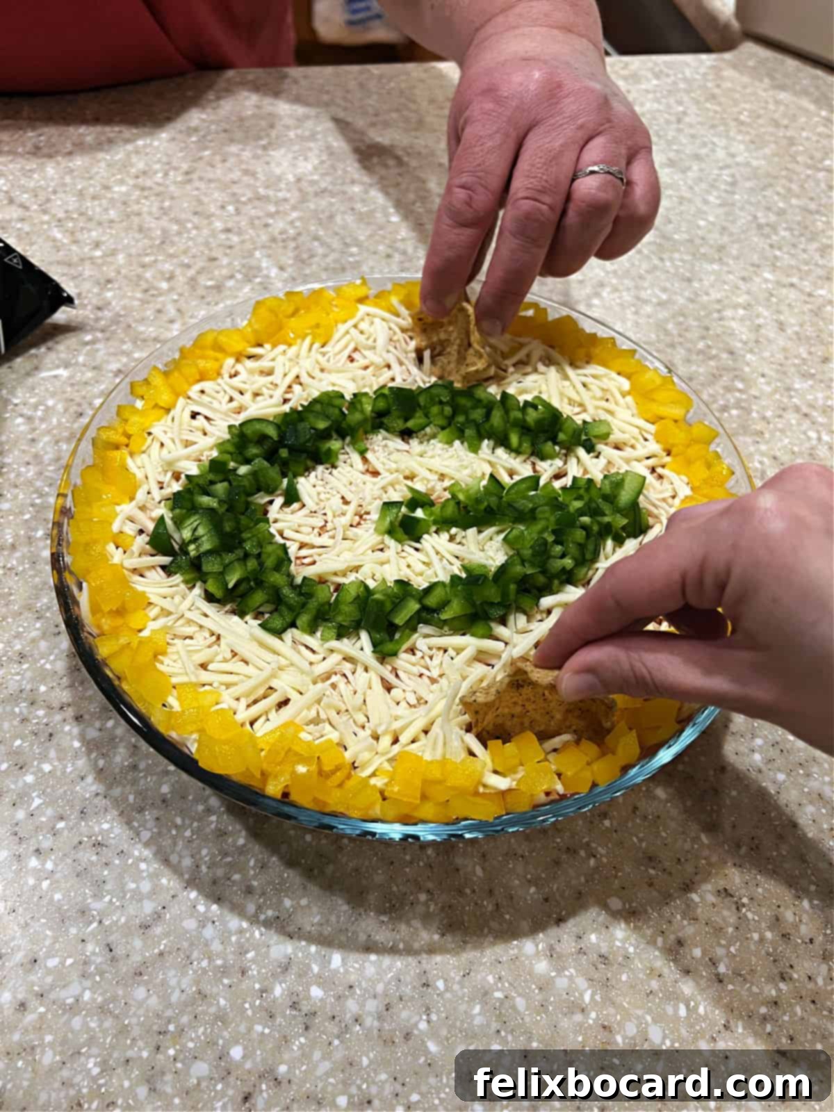 Two hands reaching in with tortilla chips to scoop a generous portion of the festive Green Bay Packers Layered Taco Dip, ready to enjoy.