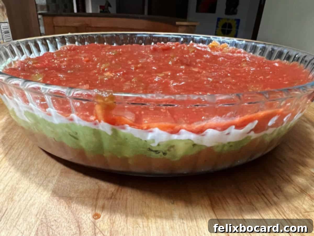 Close-up of a layered taco dip, showing a clean separation between the sour cream and salsa layers, prepared for the top decorative elements.