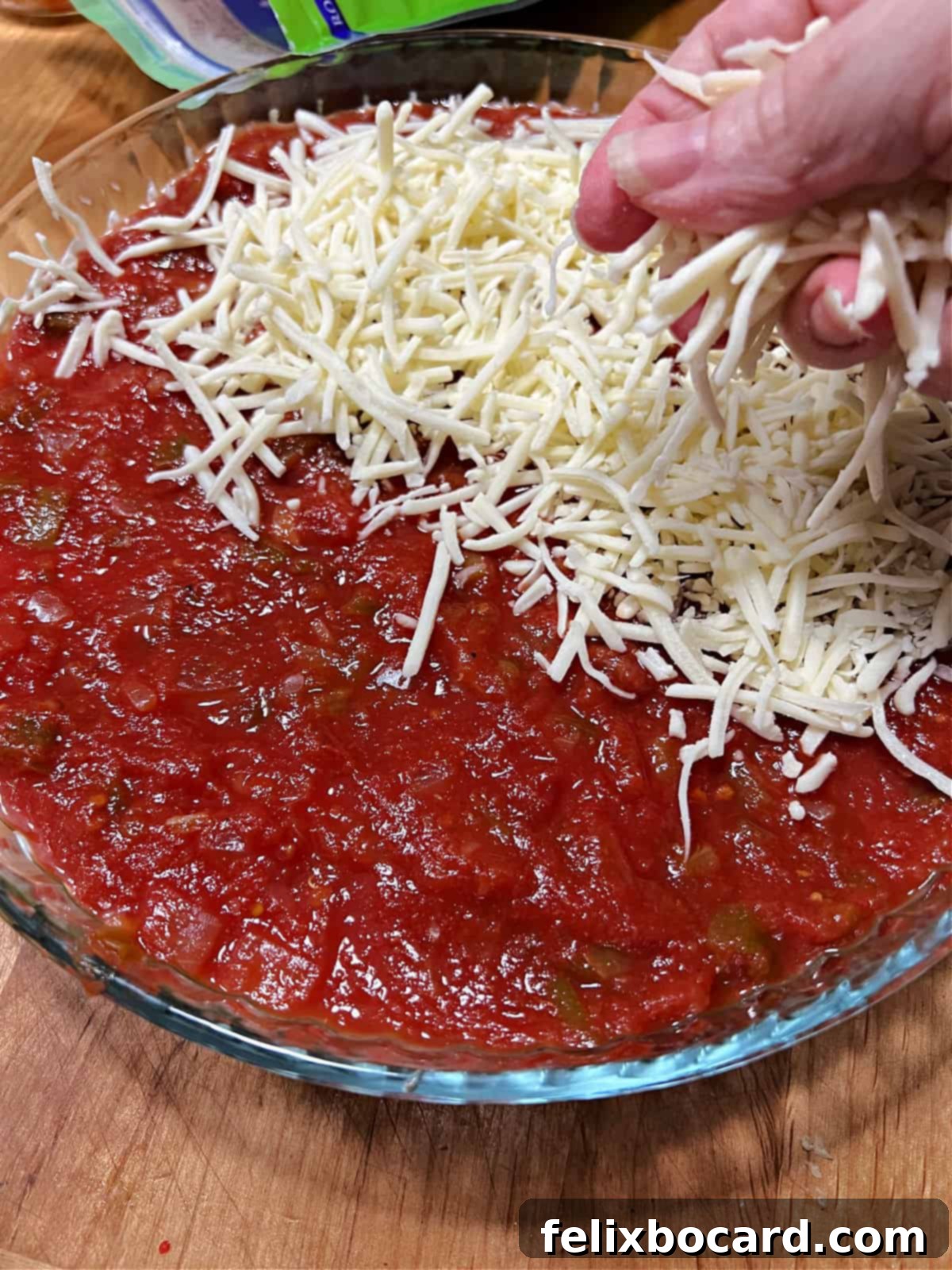 A hand evenly spreading a generous layer of shredded Monterey Jack cheese over the surface of a layered taco dip, creating a perfect canvas for decoration.