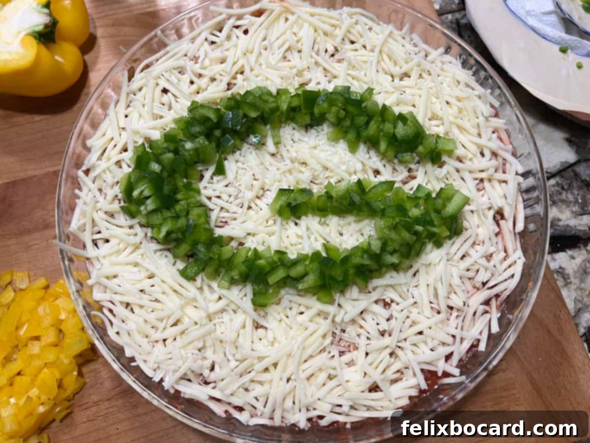 A completed Layered Taco Dip featuring the Green Bay Packers 'G' logo meticulously crafted from chopped green bell peppers on a bed of cheese.