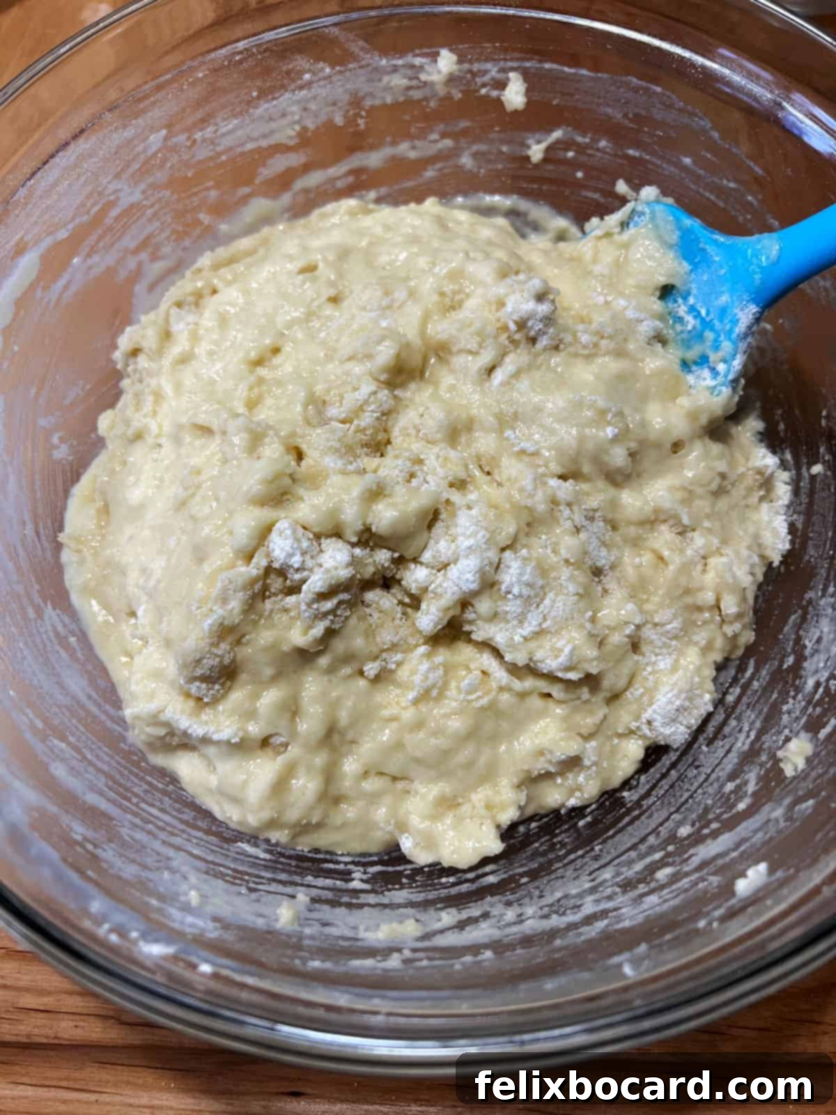 Muffin batter in a glass bowl, with a few streaks of dry flour remaining, indicating it's almost mixed but not overmixed.