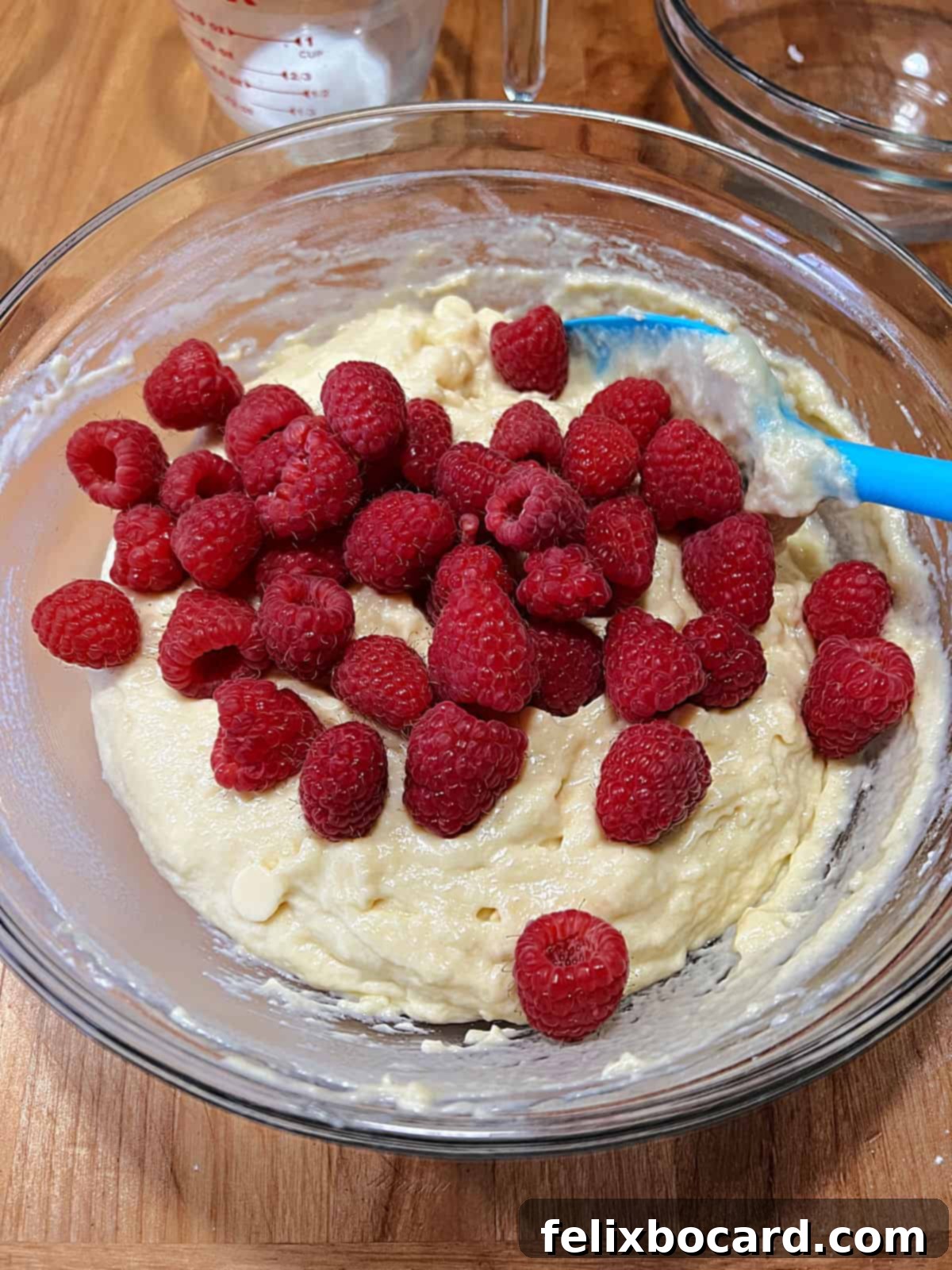 Fresh raspberries and white chocolate chips have just been added to the muffin batter in a bowl, ready for a final gentle fold.
