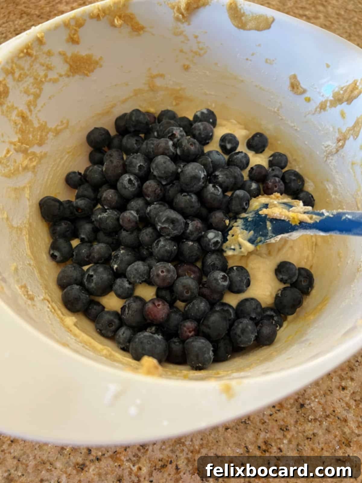 Fresh blueberries being gently added to a bowl of prepared muffin batter, ready for folding.