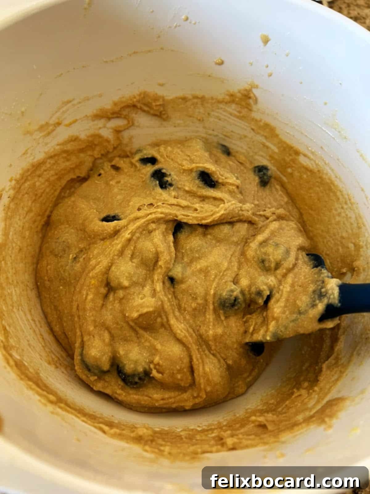 Blueberries and lemon zest perfectly mixed into the golden muffin batter, showing even distribution.