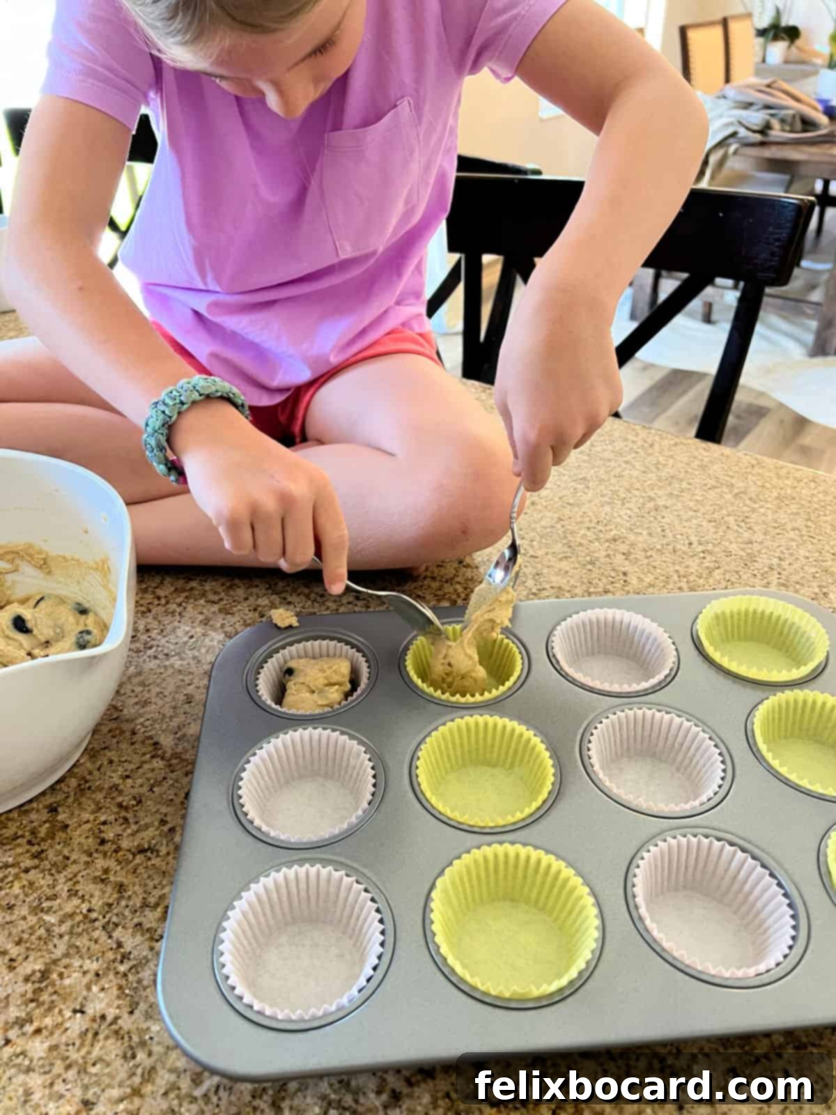 Muffin batter being carefully divided into paper-lined muffin cups in a baking tin.