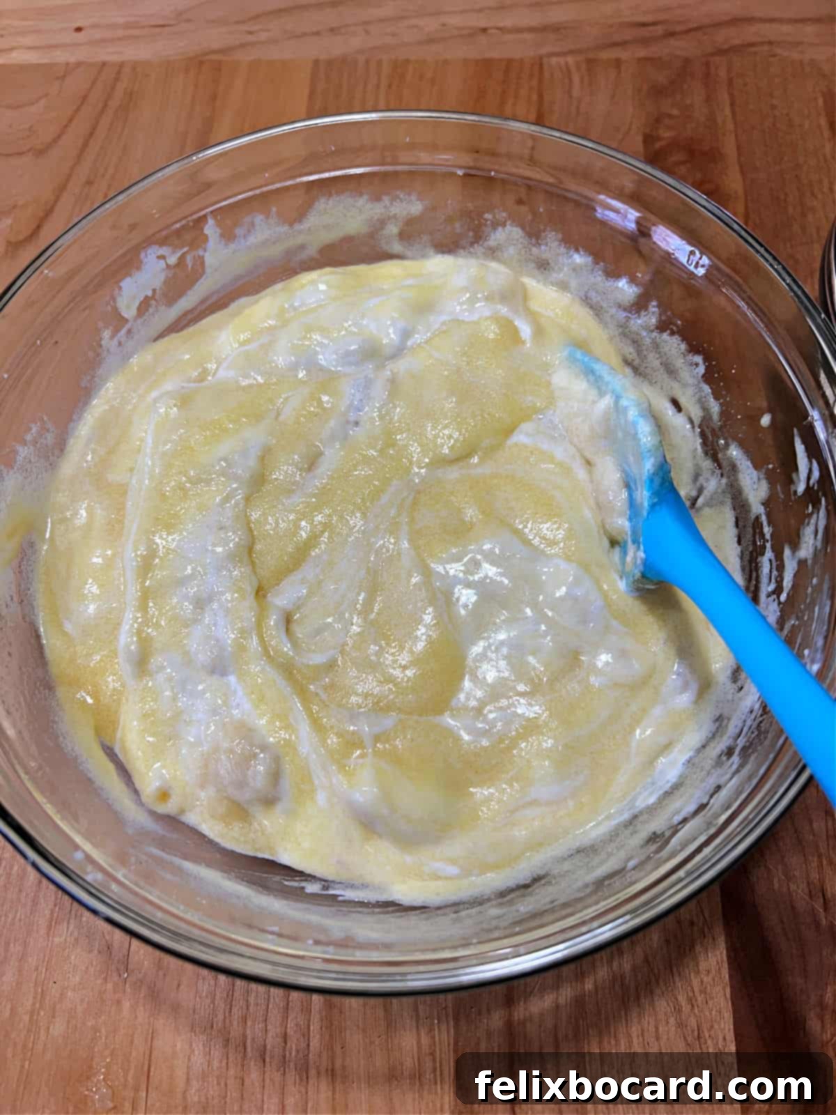 A close-up shot of creamy sour cream and mashed banana mixture being carefully added to a large mixing bowl filled with the creamed butter, sugar, and egg base, indicating the next step in preparing delicious banana bread muffins.