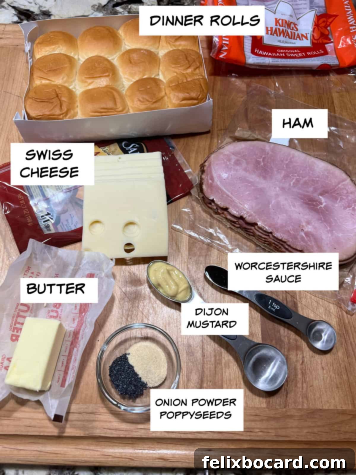 Hawaiian Ham and Cheese Sliders 3 A flat lay image displaying all ingredients needed for ham and cheese sliders: a pack of dinner rolls, sliced ham, Swiss cheese slices, a small bowl of melted butter, Dijon mustard, onion powder, poppy seeds, and Worcestershire sauce.