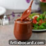 A spoon dripping strawberry balsamic vinaigrette dressing into a small jar.