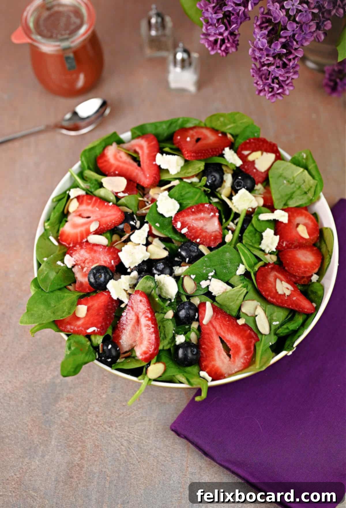 Spinach salad ready to serve with  jar of strawberry balsamic dressing nearby, ready to use.