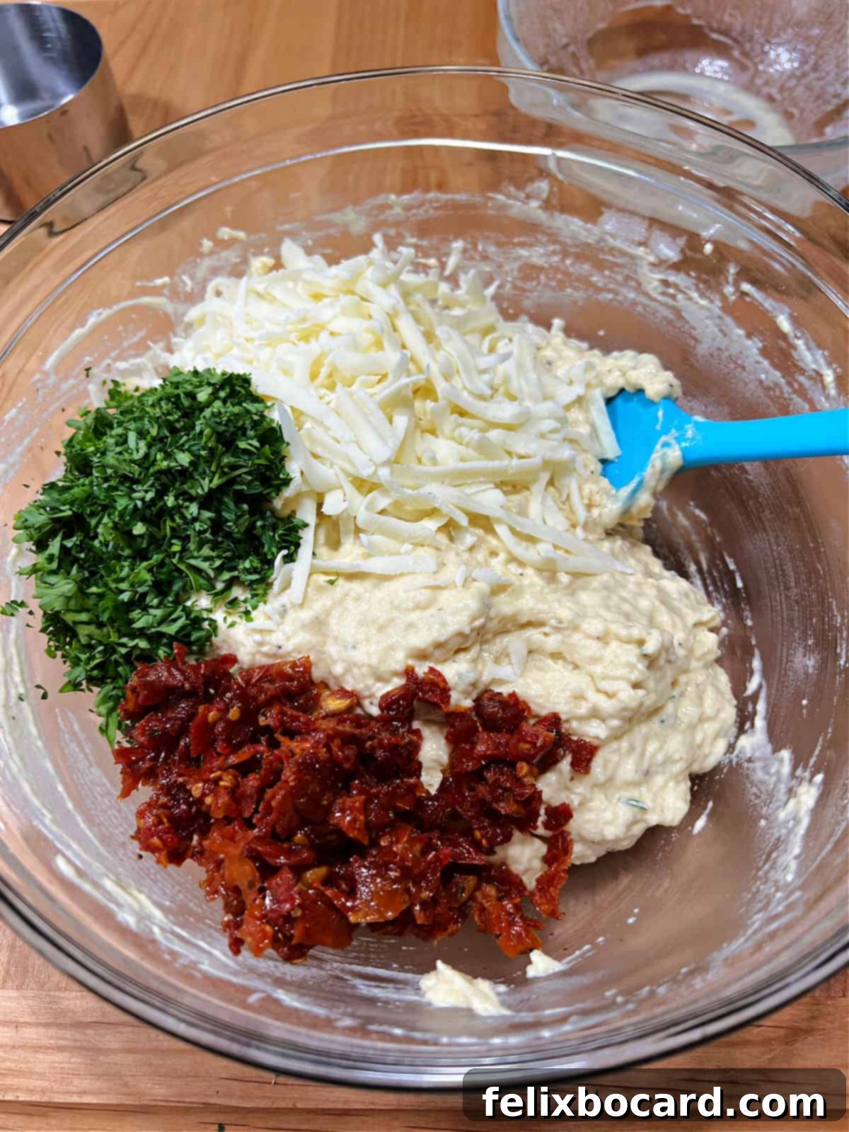 Savory Sun Dried Tomato Quick Bread 5 Shredded cheese, chopped fresh herbs, and sun-dried tomatoes being added to the bread batter in a mixing bowl.