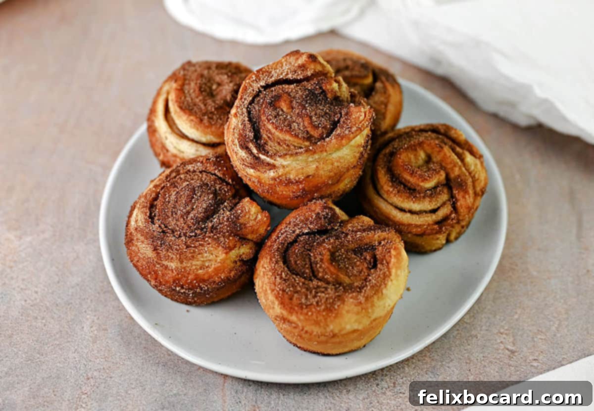 A stack of 6 golden-brown cinnamon puff pastry cruffins on a small plate, dusted with cinnamon sugar.