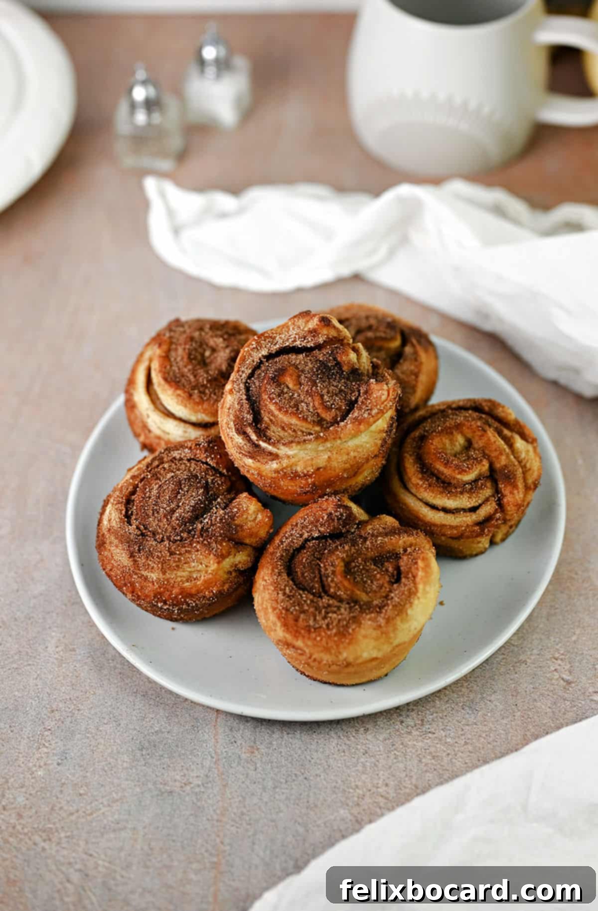 Six cinnamon cruffins, fresh out of the oven, displayed on a small white plate.