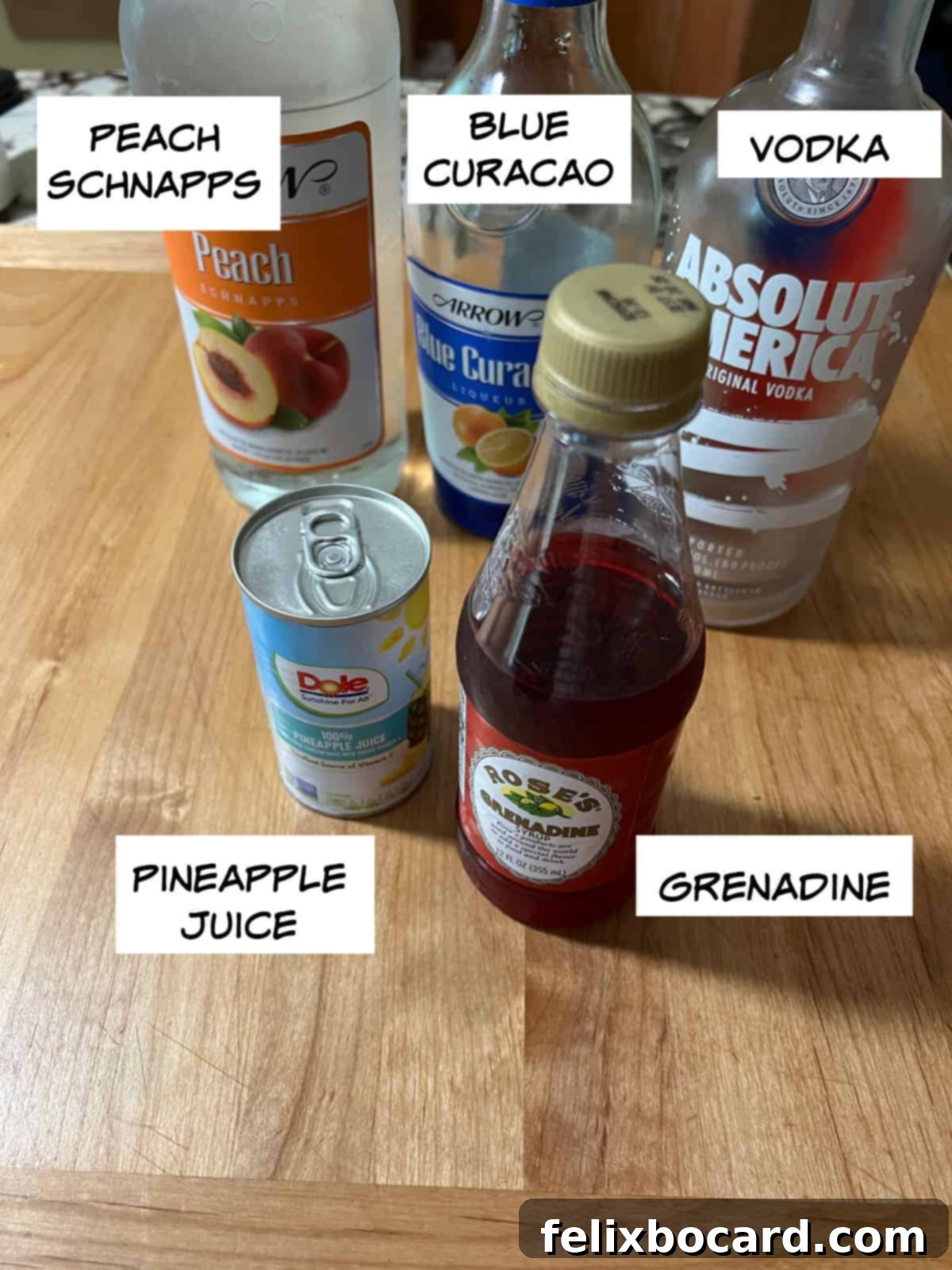Ingredients for a Rainbow Martini: peach schnapps, blue curacao, vodka, grenadine, pineapple juice laid out on a table.