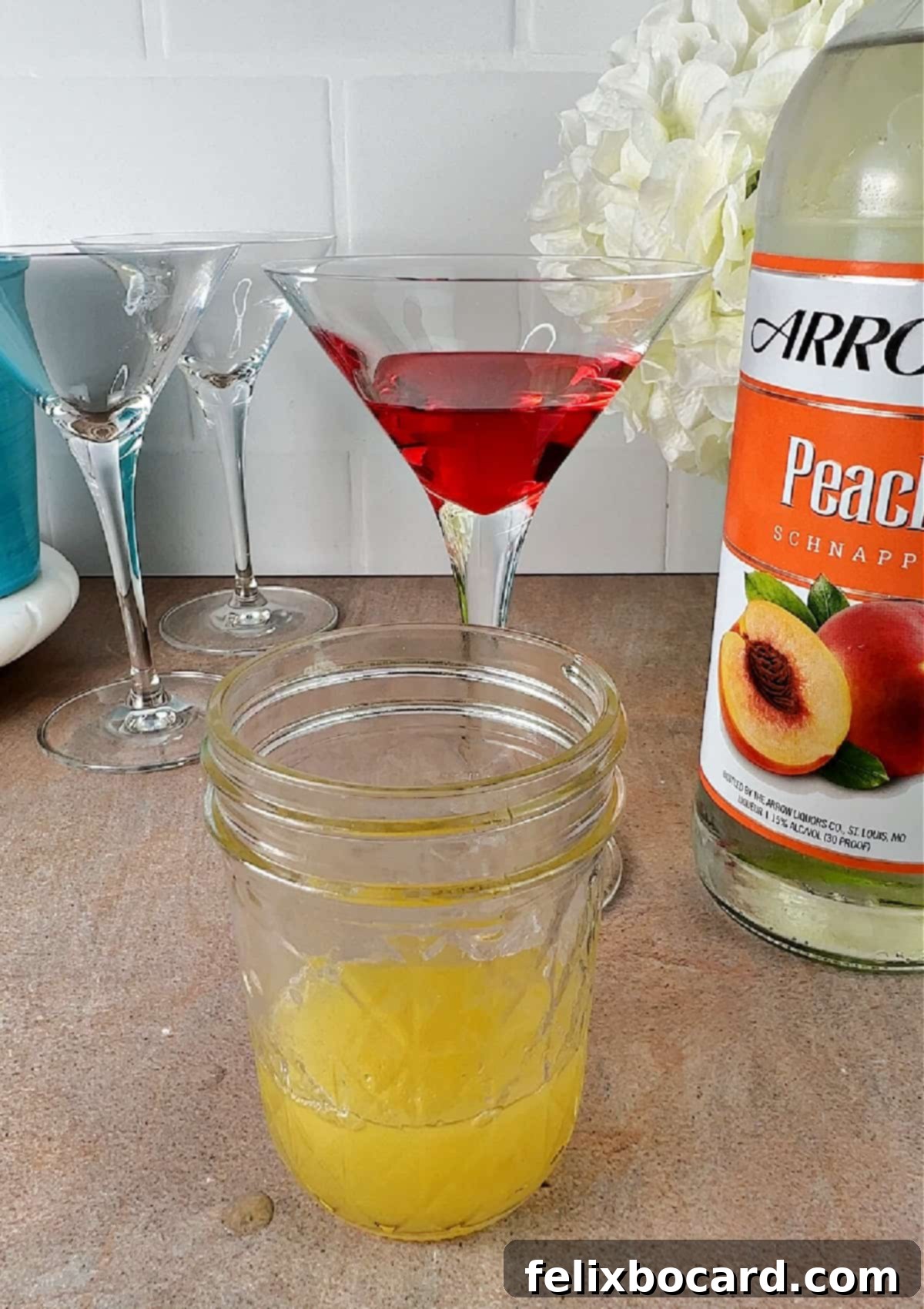 Martini glass holding grenadine behind a jelly jar holding the pineapple juice-peach schnapps mixture, illustrating the first two layers.