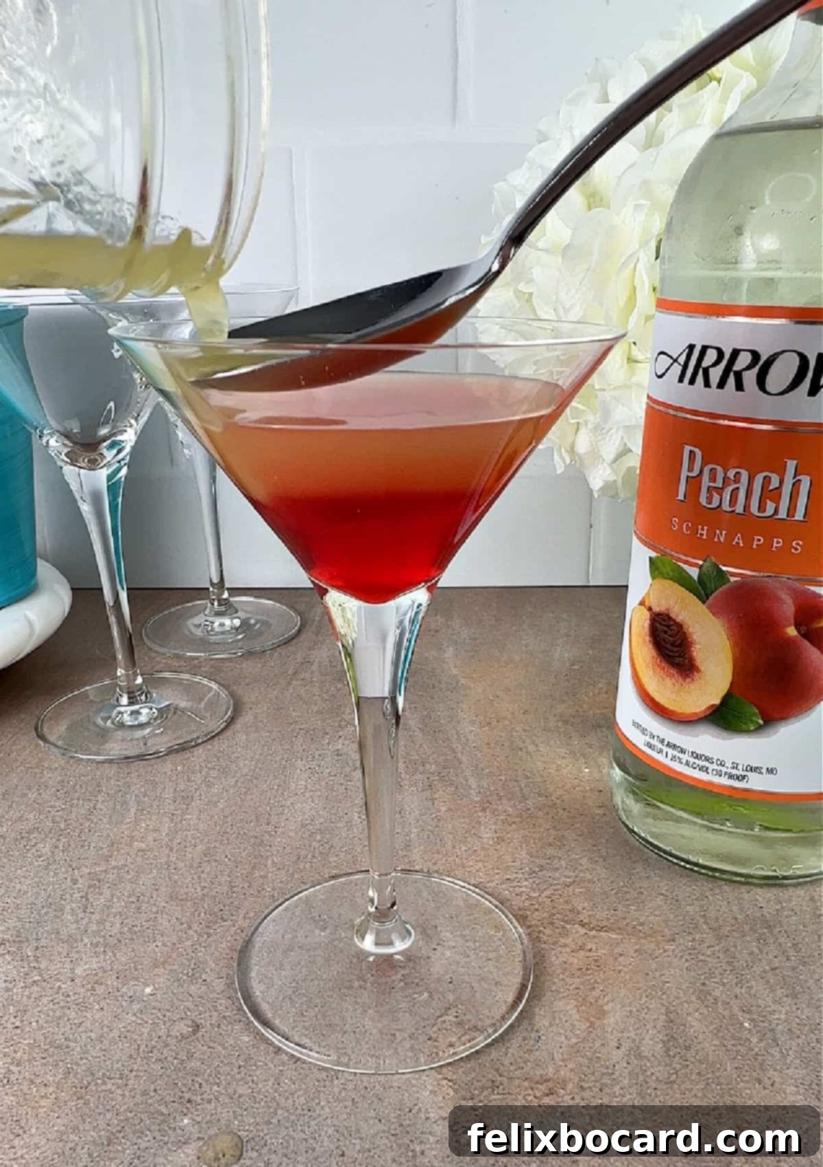 Pouring pineapple layer into the martini glass using a spoon to slow down the pour, demonstrating the layering technique.