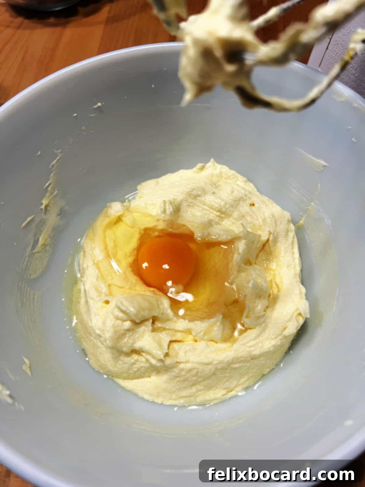 Adding an egg to the creamy muffin batter in a mixing bowl, illustrating the step-by-step process.
