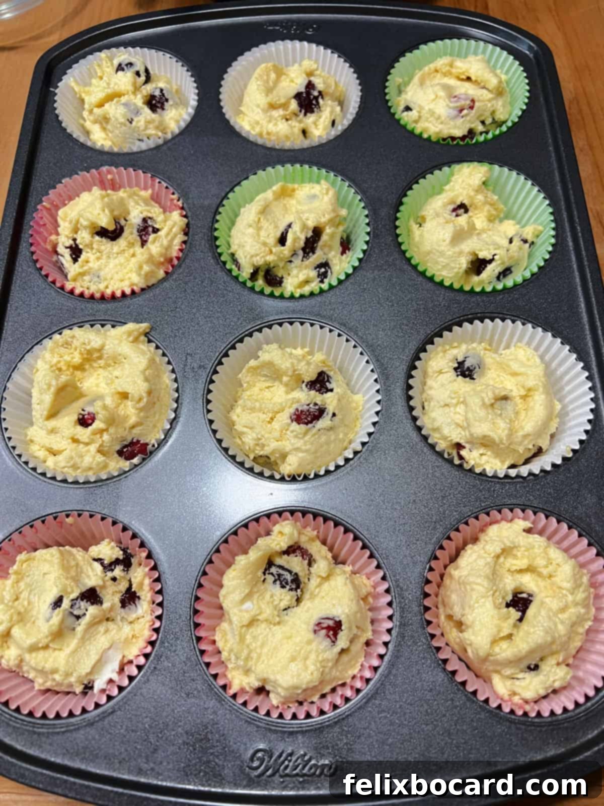 Muffin pan filled with cranberry cream cheese muffin batter in paper liners, ready to be baked to golden perfection.