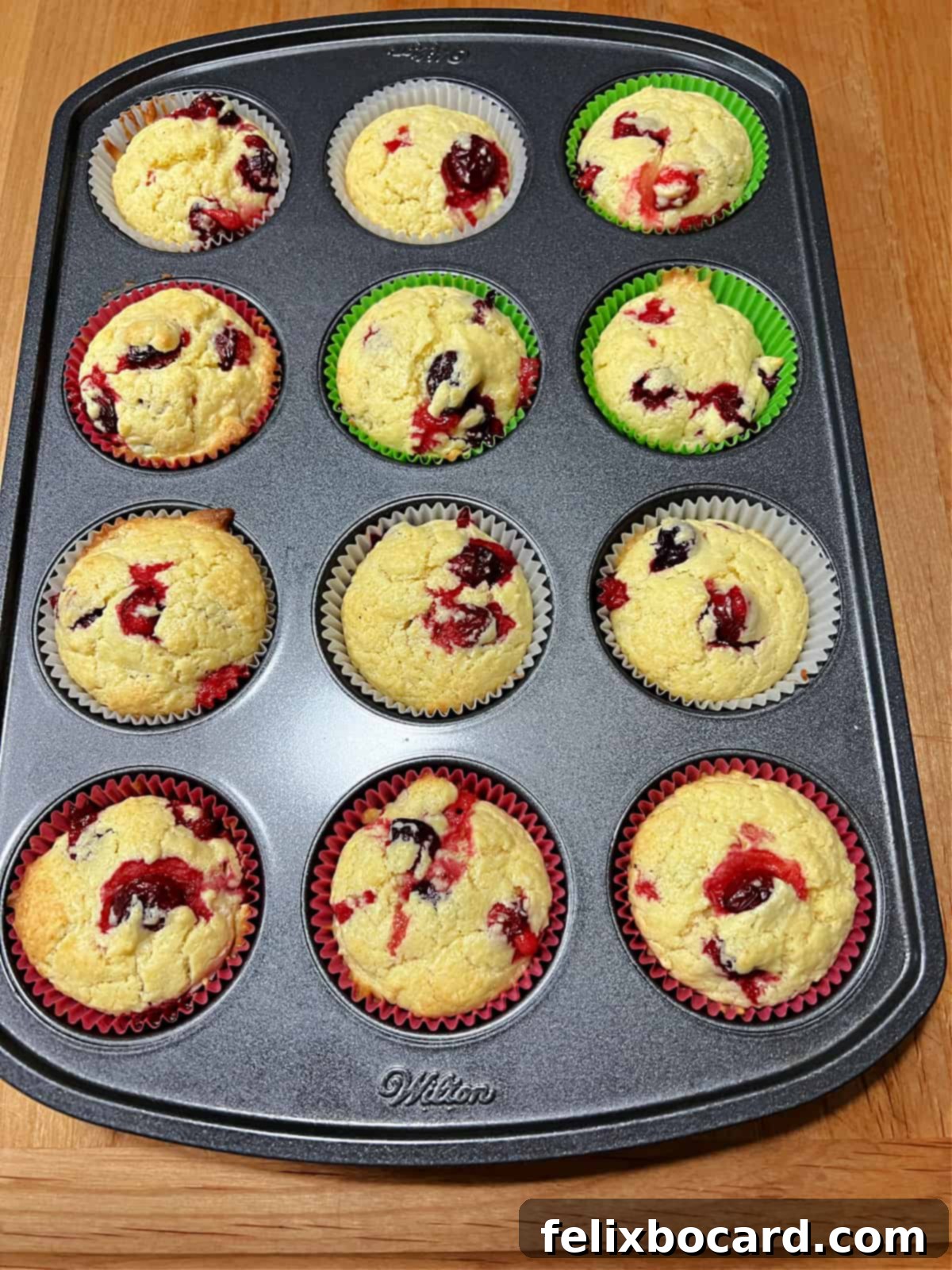 A baking pan filled with freshly baked cranberry cream cheese muffins, golden-brown and inviting, some with a light glaze.