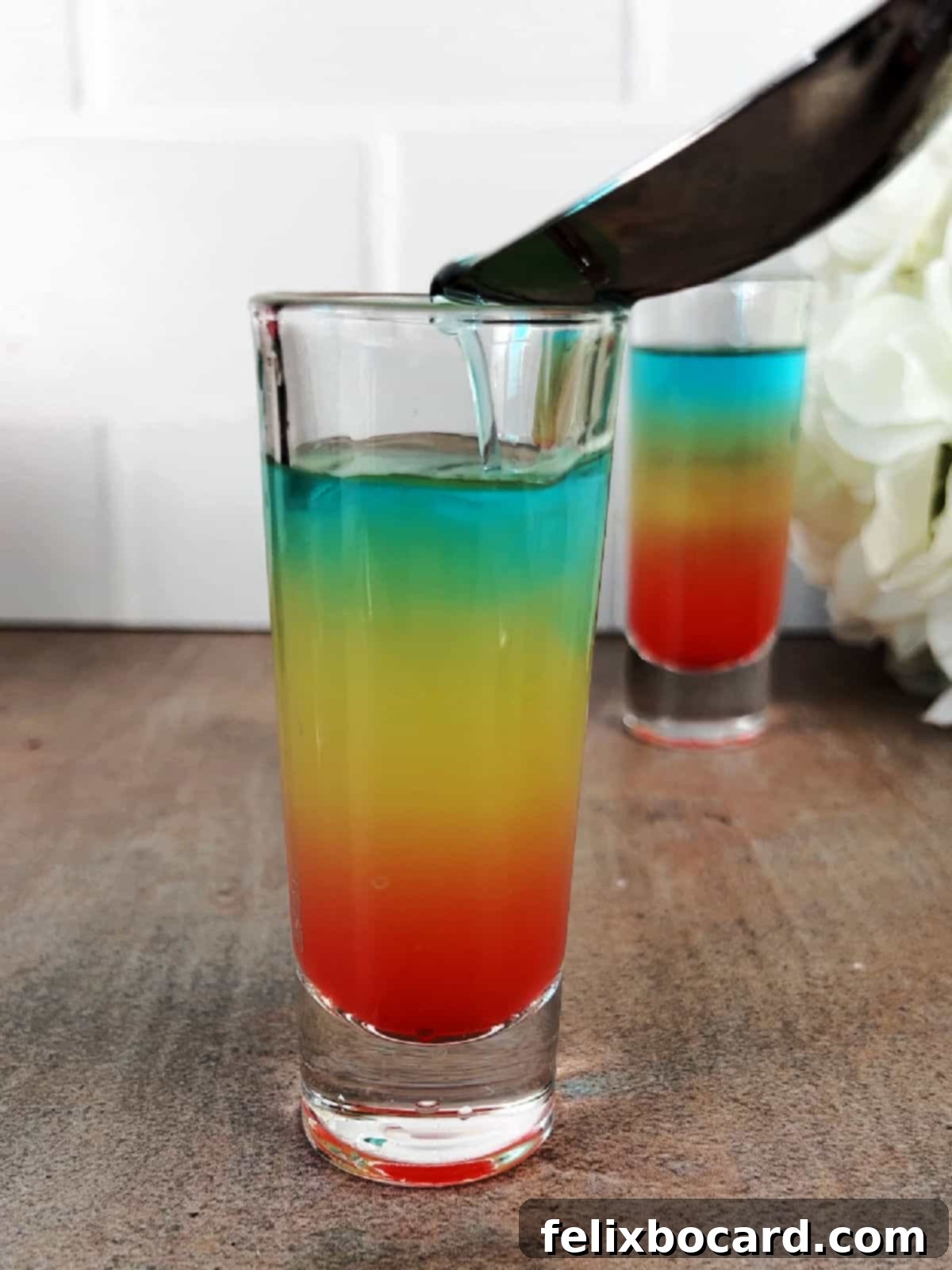 Using a spoon to carefully add the blue raspberry vodka layer on top.