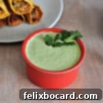 Cilantro-Lime Sauce 4 Cilantro Lime sauce in a small red bowl with taquitos behind it