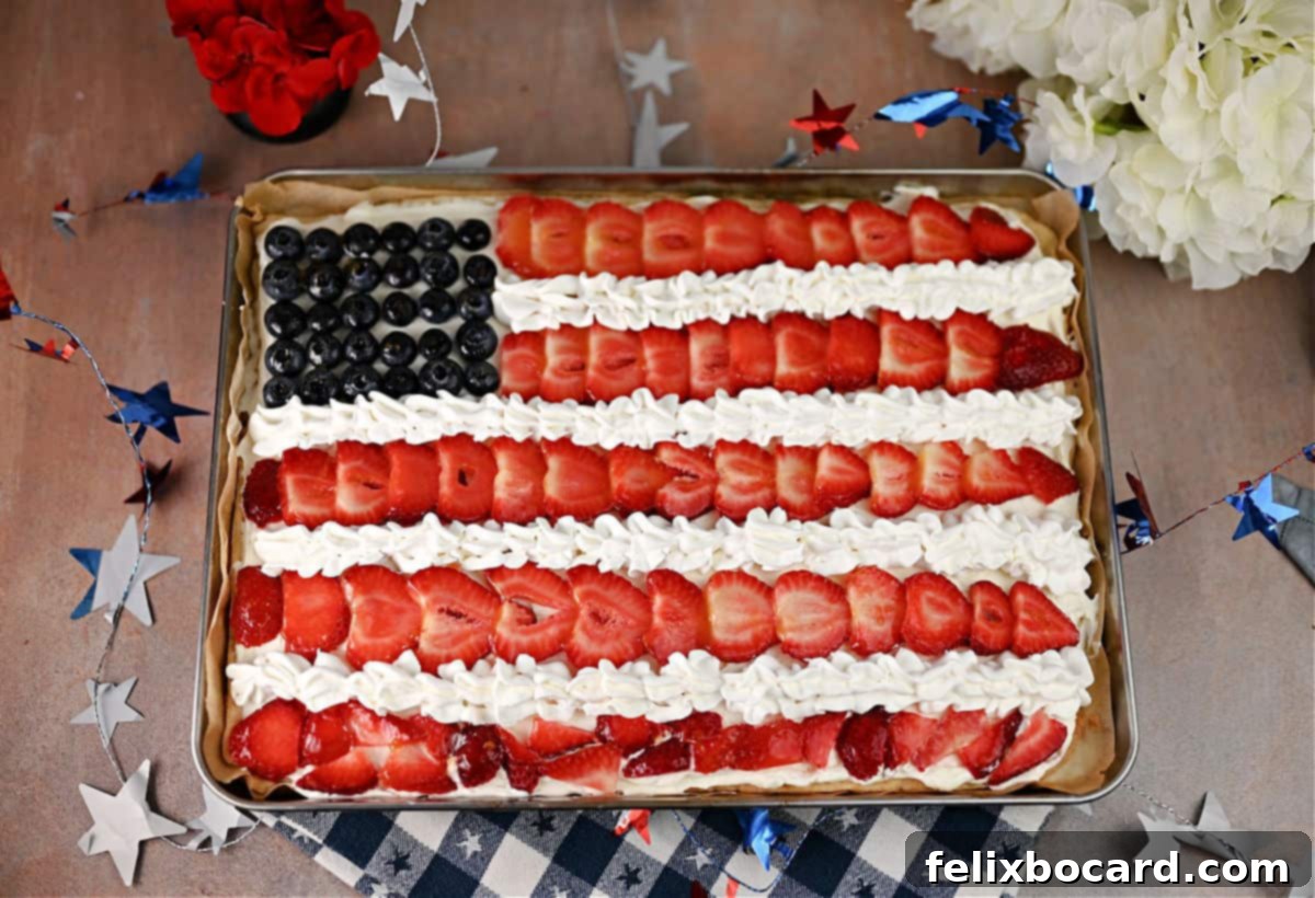 A vibrant American Flag Fruit Pizza, decorated with fresh strawberries and blueberries on a creamy white frosting base.