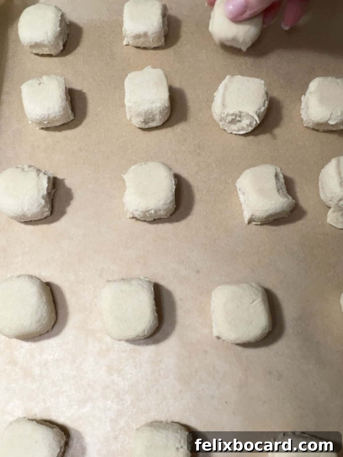 Sugar cookie dough pieces spaced out on a parchment-lined baking sheet, ready to be pressed.