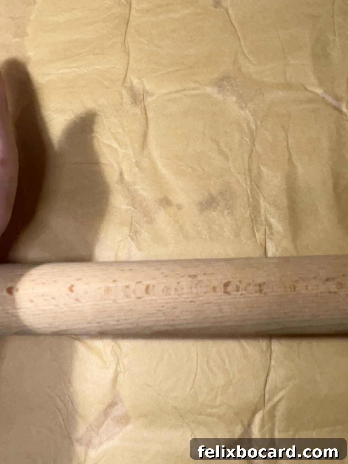 Using a rolling pin over a sheet of parchment paper to press cookie dough into a solid, even crust on a baking sheet.