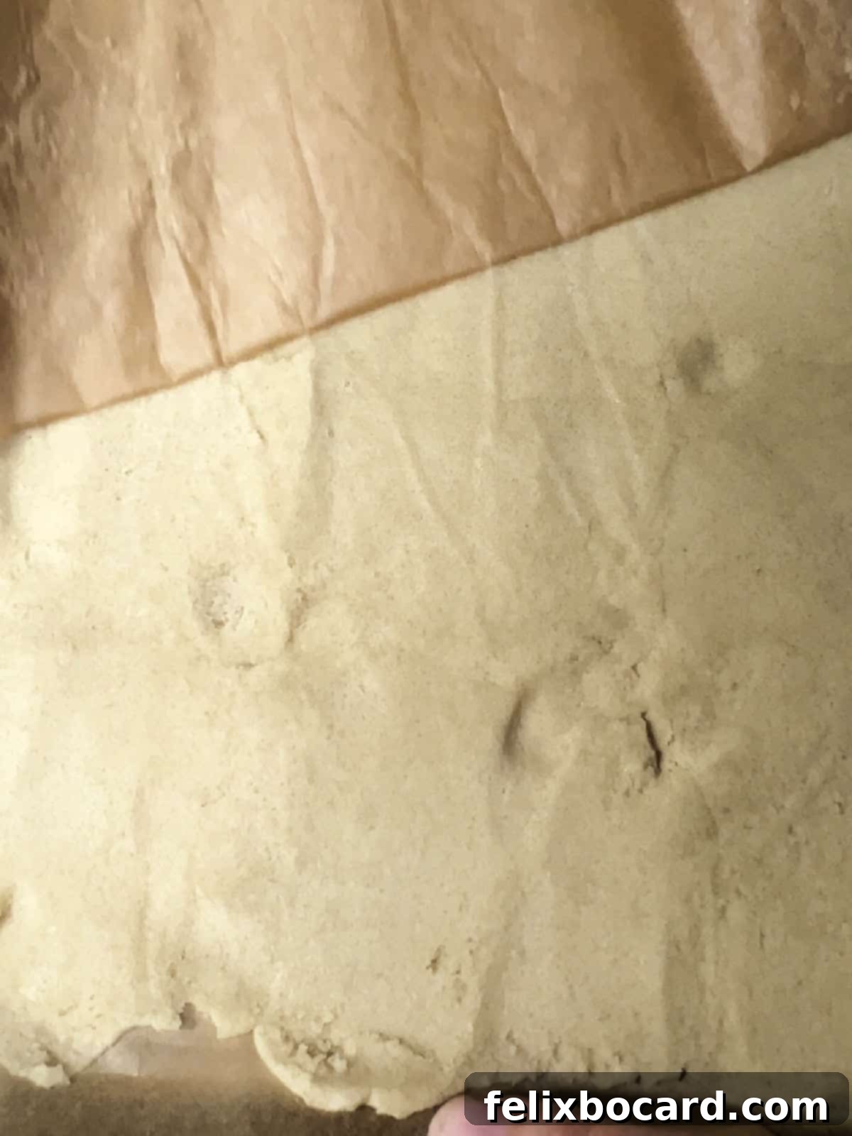 The top piece of parchment paper being peeled off the perfectly rolled sugar cookie dough crust, revealing a smooth surface.