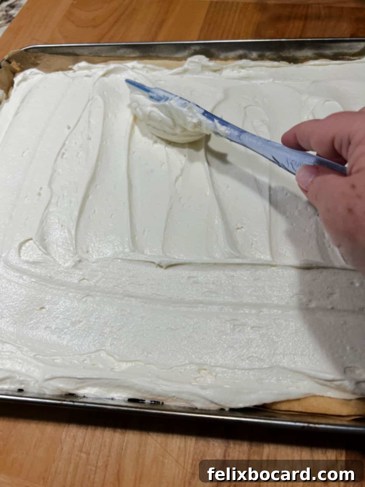 Cream cheese frosting being spread evenly across the golden-baked sugar cookie crust.