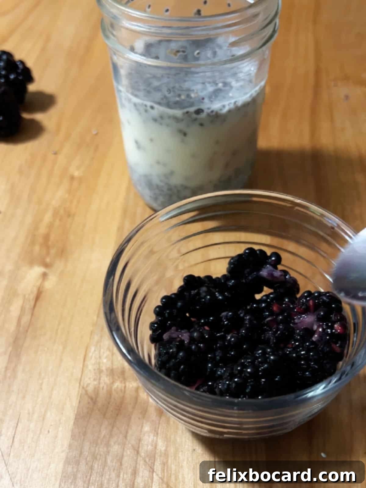 Fresh blackberries being lightly mashed in a small bowl with a fork.