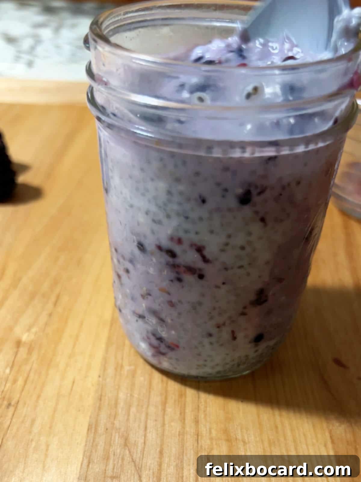 Blackberries added to the chia seed mixture and being stirred well to evenly distribute the seeds and fruit.