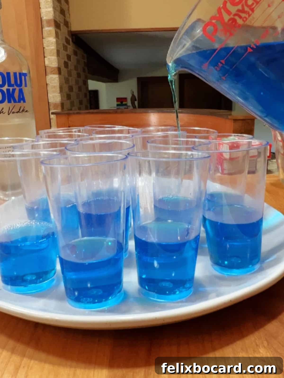 Pouring blue jello layer into the shot glasses on a white tray.