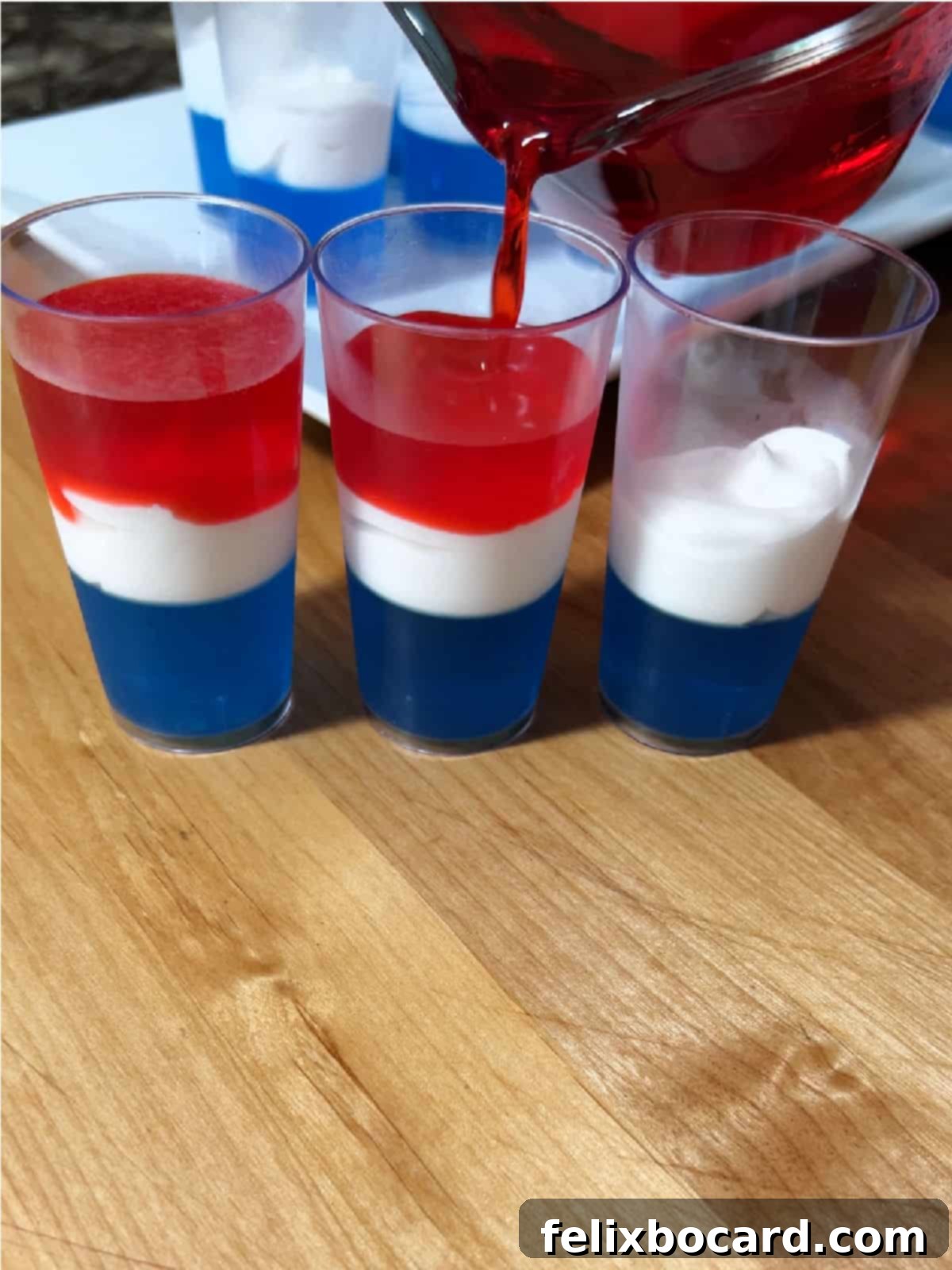 Slowly pouring the red jello layer on top of the white and blue layers in the shot glasses.