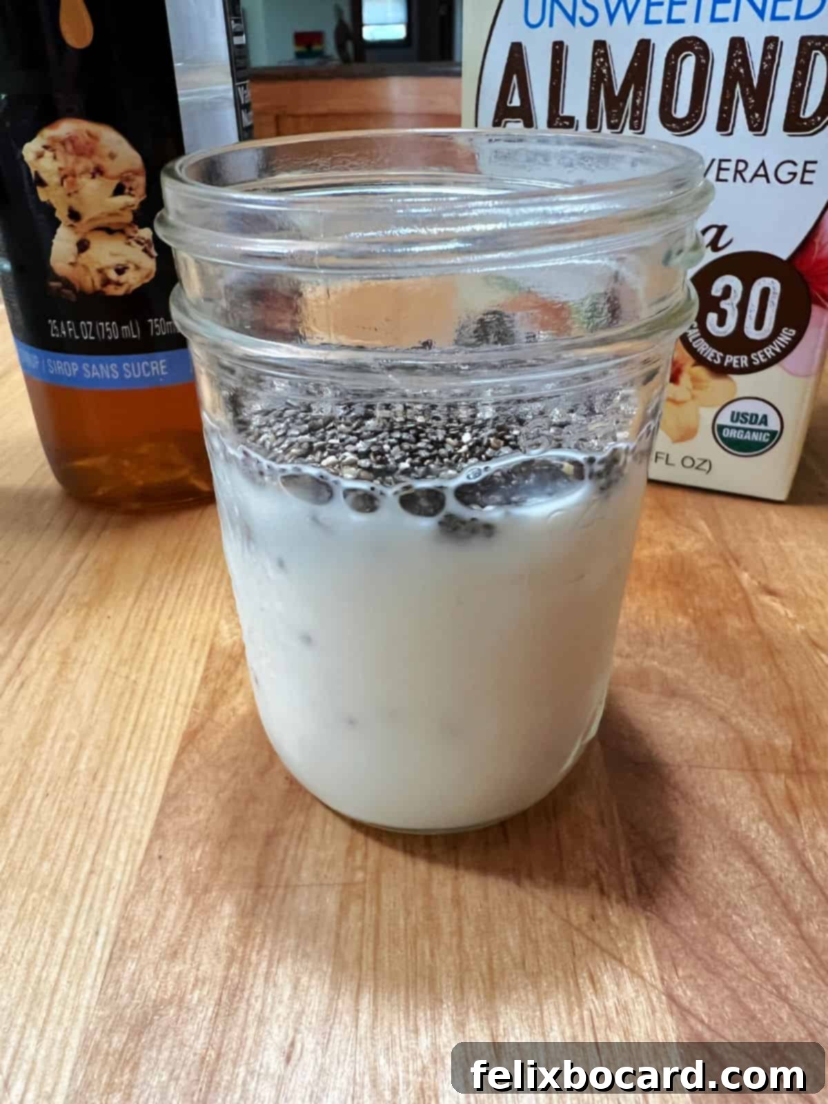 Almond milk and chia seeds being stirred together in a small glass jar to begin the pudding preparation.
