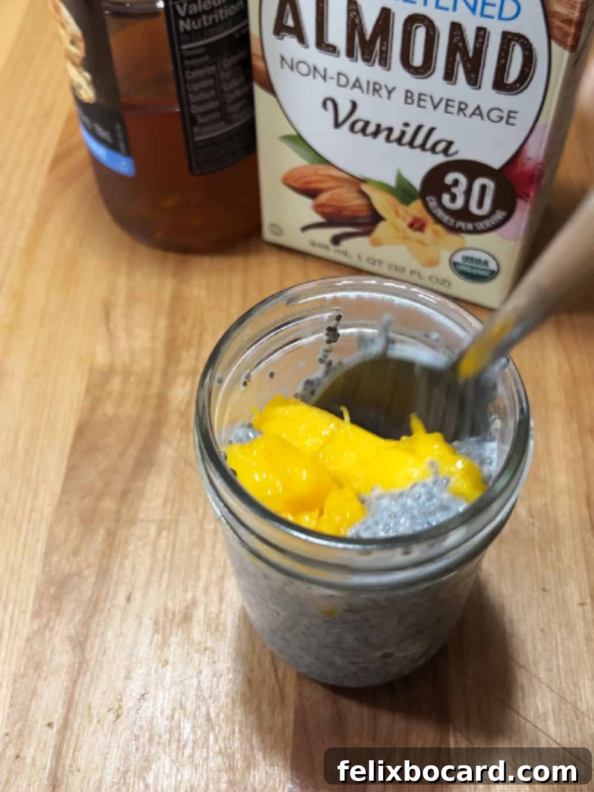 Diced fresh mango pieces added to the chia seed and milk mixture in a jar.