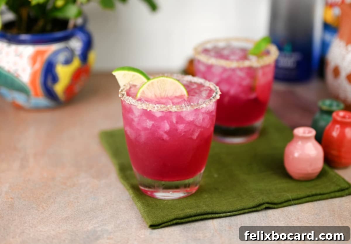 Two vibrant prickly pear margaritas garnished with fresh lime slices, ready to be enjoyed.