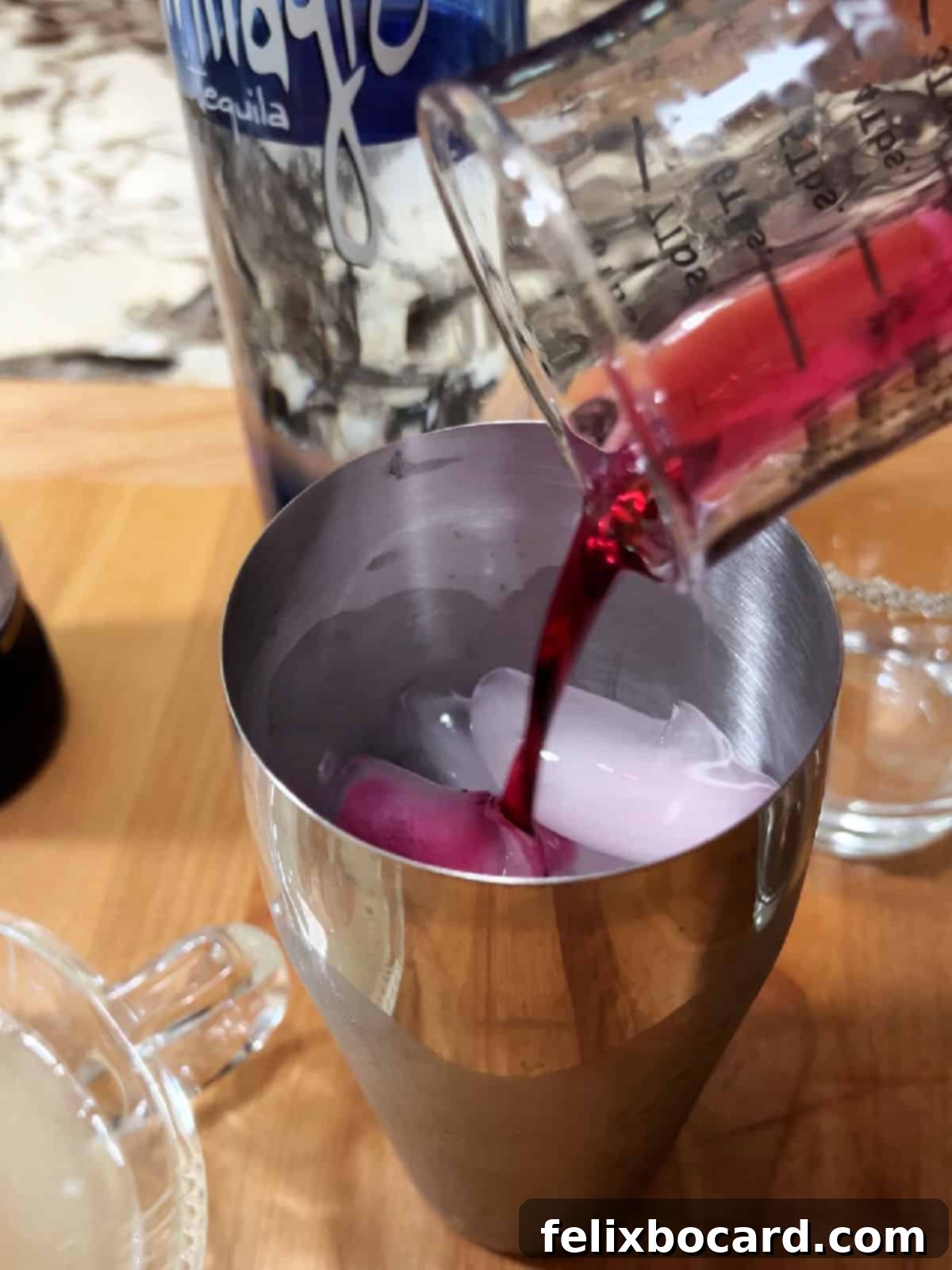 A cocktail shaker being filled with prickly pear syrup, other ingredients, and ice, ready for mixing.